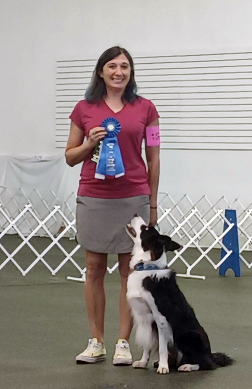 Sally Gordon holding her border collie's first place ribbon as he looks on.